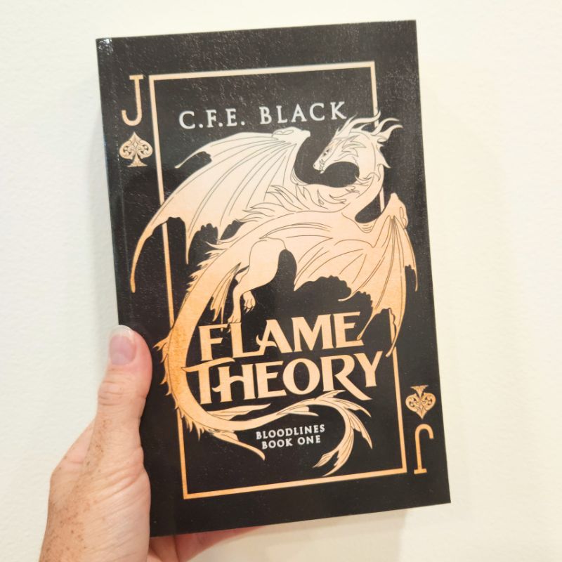 Flame Theory paperback with black and gold glossy cover featuring a dragon and playing card motif.