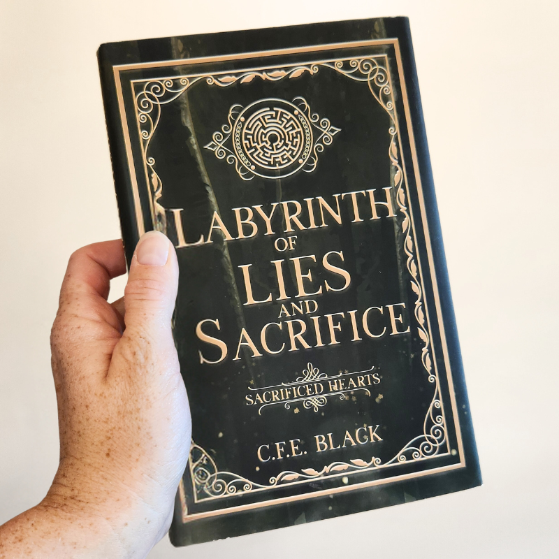 Labyrinth of Lies and Sacrifice hardback in hand