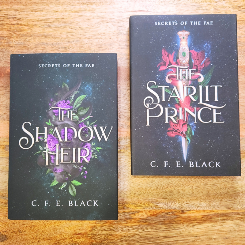 Two no-spice romantasy hardcover books titled 'The Shadow Their' and 'The Starlit Prince' by C. F. E. Black on a wooden surface.