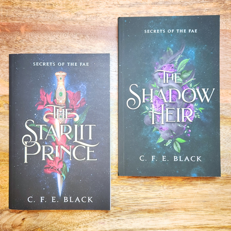 Two no-spice romantasy books titled 'The Starlit Prince' and 'The Shadow Heir' by C. F. E. Black on a wooden surface.